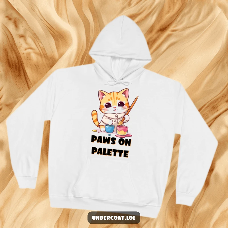 Funny hoodie with a curious cat wearing a smock and dipping a brush into paint, designed for cozy creative sessions.